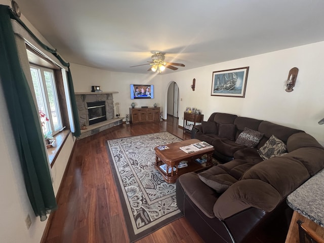 living room featuring dark wood finished floors, a fireplace, arched walkways, and ceiling fan