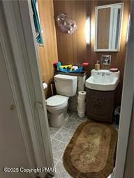 half bathroom featuring toilet, wood walls, vanity, and tile patterned flooring