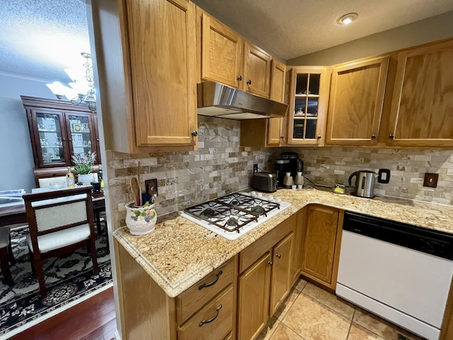 kitchen with a textured ceiling, under cabinet range hood, white appliances, tasteful backsplash, and glass insert cabinets