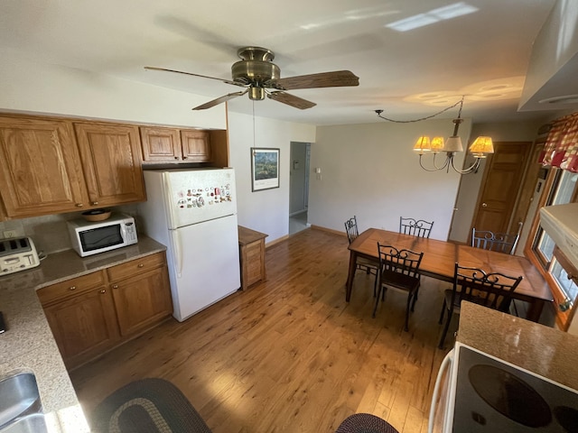 kitchen featuring brown cabinets, ceiling fan with notable chandelier, light wood finished floors, and white appliances