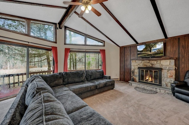 living area featuring beam ceiling, a stone fireplace, wood walls, light colored carpet, and ceiling fan