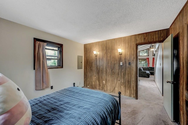 bedroom featuring light carpet, wood walls, a textured ceiling, and multiple windows