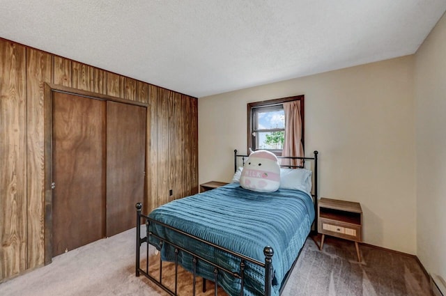 bedroom featuring a closet, light carpet, a textured ceiling, and wood walls