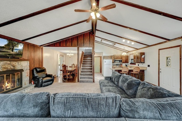 living area featuring stairway, light colored carpet, lofted ceiling with beams, ceiling fan with notable chandelier, and a fireplace