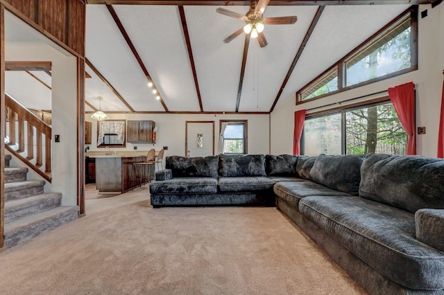 living area featuring beam ceiling, a ceiling fan, light colored carpet, a healthy amount of sunlight, and stairs