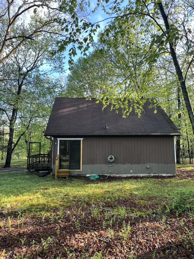 view of side of property featuring a shingled roof, a wooden deck, and a lawn