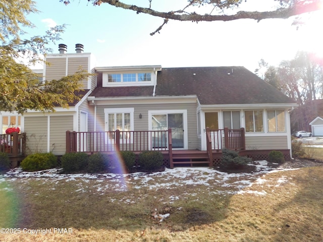 snow covered rear of property with a chimney, a sunroom, and a deck