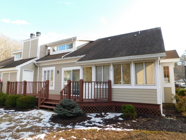 snow covered property featuring a deck, a shingled roof, and a chimney