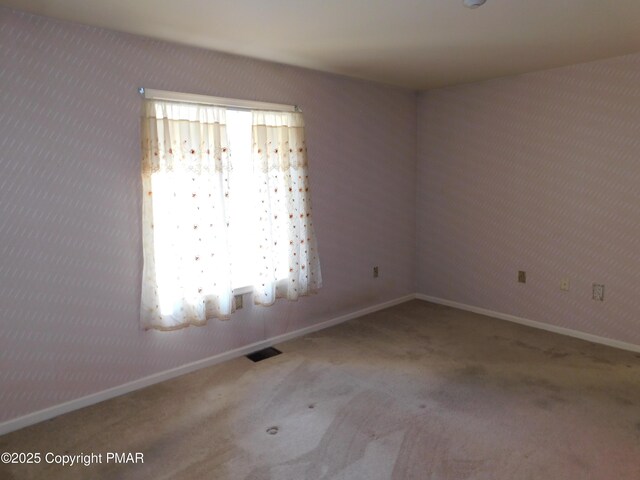 spare room with carpet flooring, visible vents, and baseboards