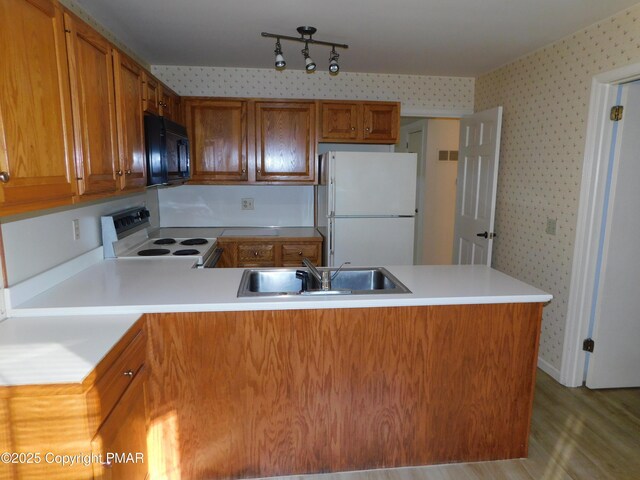 kitchen with a peninsula, white appliances, a sink, and wallpapered walls