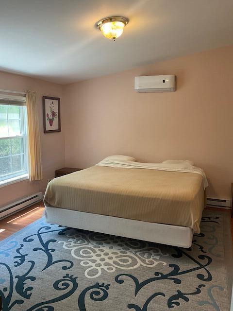 3124 Bluebird Dr, Bushkill, PA 18324 - bedroom with a wall mounted air conditioner, wood finished floors, and baseboard heating