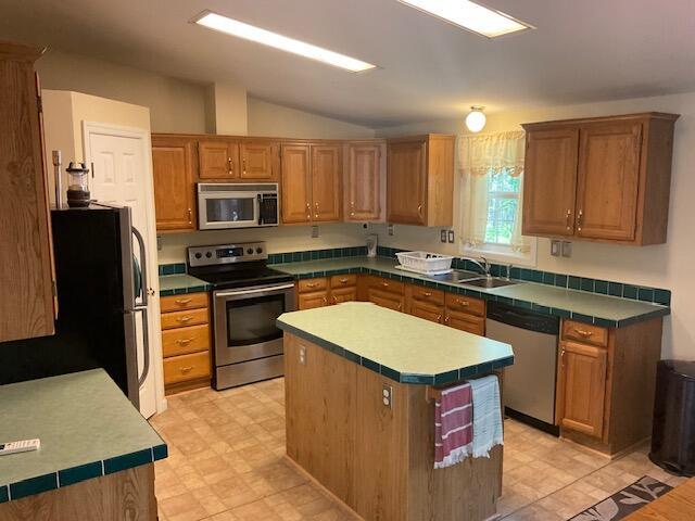 3124 Bluebird Dr, Bushkill, PA 18324 - kitchen with stainless steel appliances, a center island, vaulted ceiling, light flooring, and brown cabinets