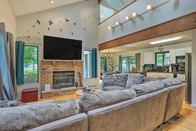 348 Fernwood Dr, East Stroudsburg, PA 18301 - living room featuring light wood-style flooring, a baseboard radiator, high vaulted ceiling, a brick fireplace, and a chandelier