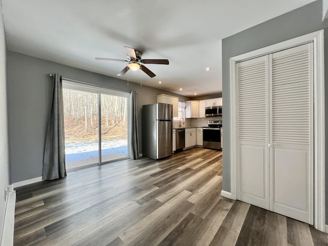 kitchen with stainless steel appliances, a ceiling fan, wood finished floors, white cabinets, and a baseboard heating unit