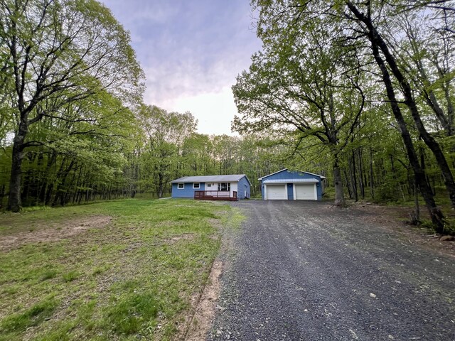 manufactured / mobile home with an outdoor structure, a detached garage, a view of trees, and a wooden deck