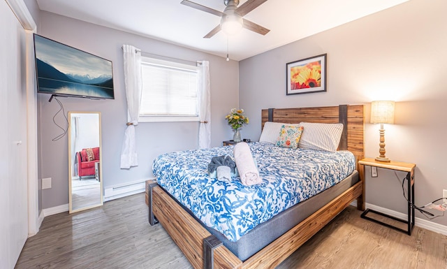 bedroom with a baseboard heating unit, ceiling fan, baseboards, and wood finished floors