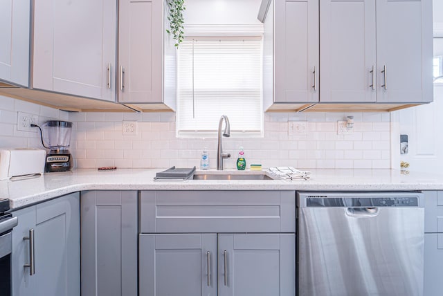 kitchen with backsplash, gray cabinetry, a sink, light stone countertops, and dishwasher