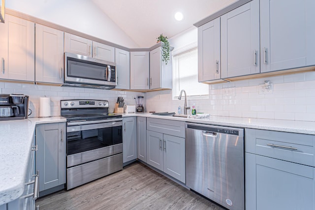 kitchen featuring lofted ceiling, stainless steel appliances, a sink, light wood-type flooring, and backsplash