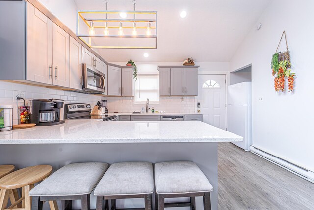 kitchen with a baseboard radiator, gray cabinetry, appliances with stainless steel finishes, a sink, and a peninsula