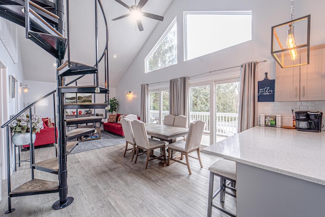 dining space featuring light wood finished floors, high vaulted ceiling, and a ceiling fan