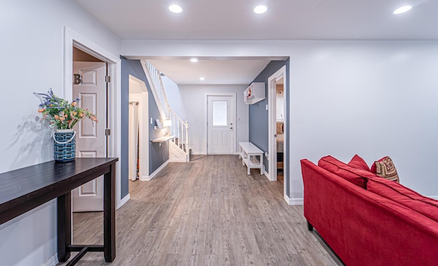 hall featuring a wall unit AC, recessed lighting, baseboards, stairway, and light wood finished floors