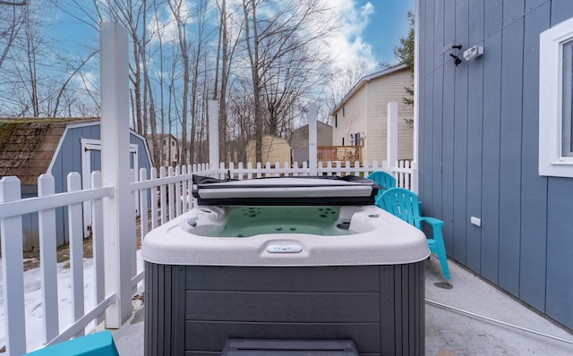 view of patio with a hot tub, fence, a storage unit, and an outdoor structure