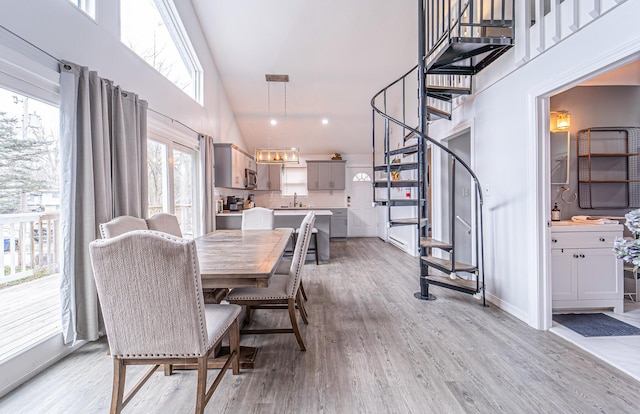 dining space featuring high vaulted ceiling, a notable chandelier, baseboards, stairs, and light wood finished floors