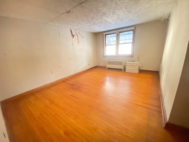 spare room featuring radiator, baseboards, and light wood finished floors