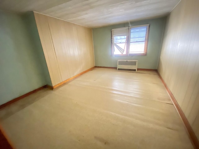 unfurnished room with baseboards, wood walls, and radiator heating unit