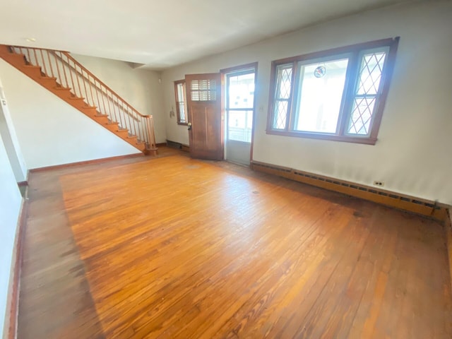 unfurnished living room with stairs, a baseboard heating unit, light wood-type flooring, and baseboards