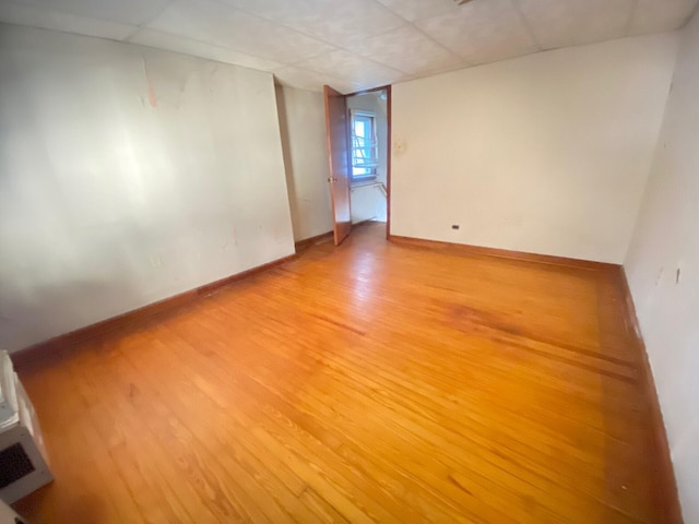 empty room with light wood-type flooring, a paneled ceiling, and baseboards