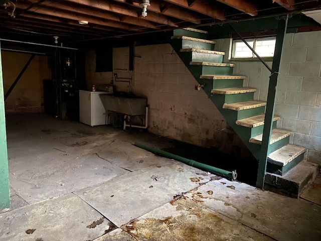 below grade area featuring stairs, a sink, washer / dryer, and concrete block wall