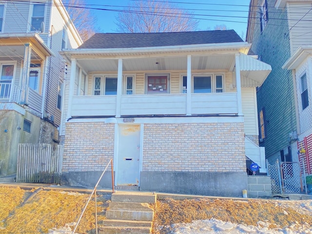 view of front of house featuring a shingled roof, fence, and brick siding