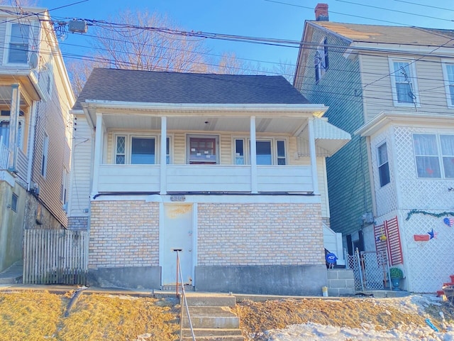 view of front of house featuring brick siding, fence, and roof with shingles