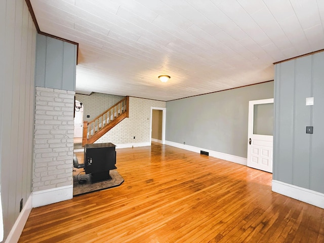 233 Lafayette Ave, Palmerton, PA 18071 - unfurnished living room featuring hardwood / wood-style floors, brick wall, a wood stove, stairway, and crown molding