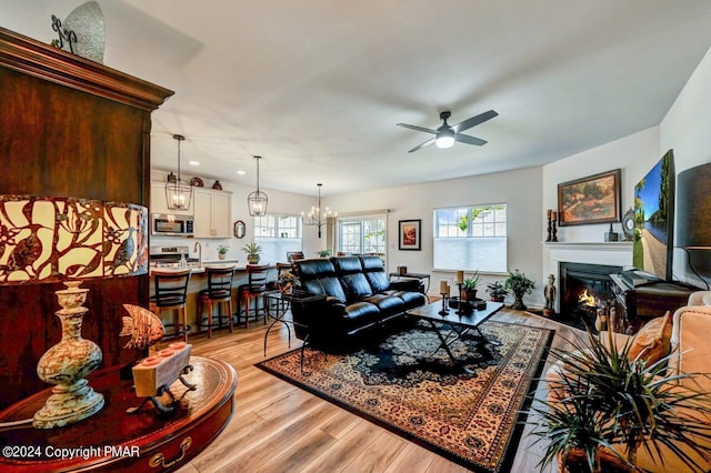 living area with light wood-style flooring, ceiling fan with notable chandelier, and a glass covered fireplace