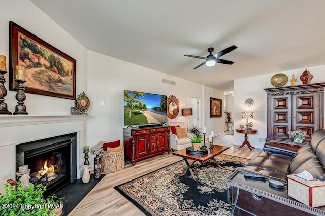 living room with light wood finished floors, visible vents, a ceiling fan, and a glass covered fireplace