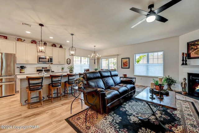 living area with recessed lighting, a glass covered fireplace, light wood-type flooring, baseboards, and ceiling fan with notable chandelier