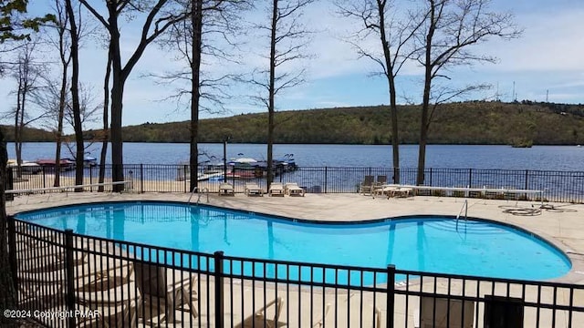 community pool featuring a water view, a patio area, and fence