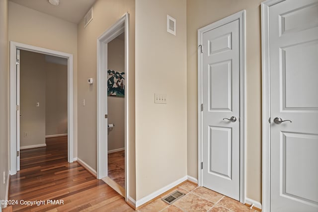 hall featuring light wood-style flooring, visible vents, and baseboards