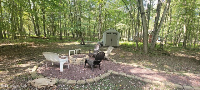 view of yard featuring a storage shed, an outdoor fire pit, a view of trees, and an outdoor structure