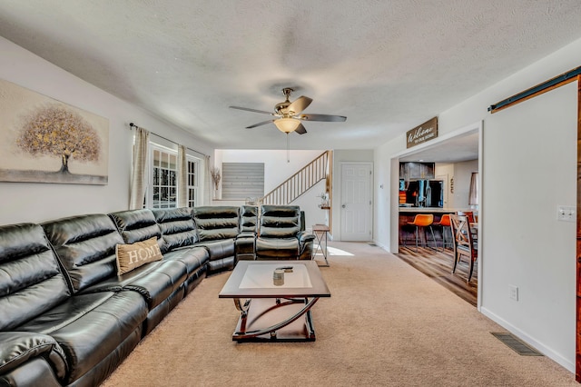 carpeted living room with stairs, a textured ceiling, visible vents, and ceiling fan