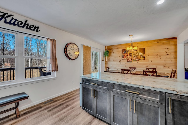 kitchen featuring light wood finished floors, a healthy amount of sunlight, wood walls, and light stone countertops