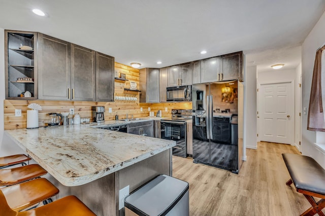 kitchen featuring black appliances, open shelves, a sink, a kitchen breakfast bar, and a peninsula