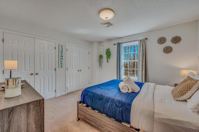 bedroom featuring visible vents, multiple closets, a textured ceiling, and carpet flooring