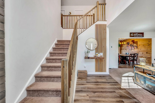 stairs featuring baseboards, wood finished floors, and a towering ceiling