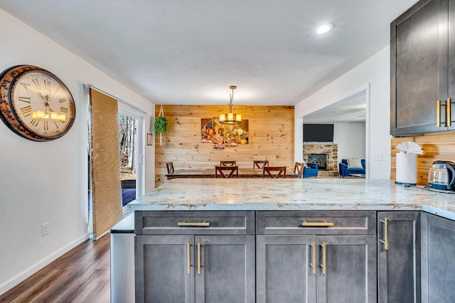 kitchen featuring dark wood-type flooring, wooden walls, a stone fireplace, a peninsula, and light stone countertops