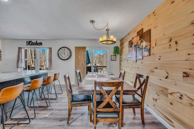 dining space featuring baseboards, wood walls, light wood-style floors, a notable chandelier, and a textured ceiling