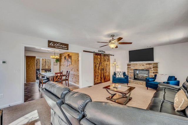 carpeted living area with baseboards, a stone fireplace, a ceiling fan, and a barn door