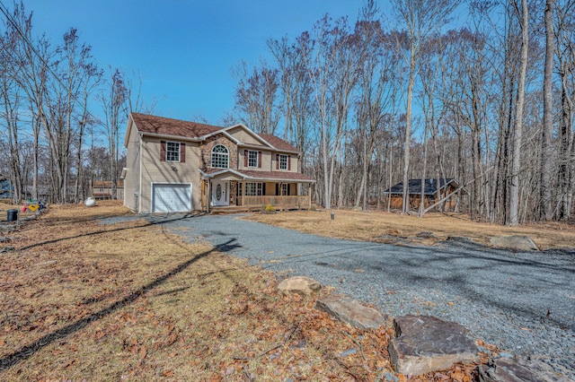 view of front of house featuring a garage, covered porch, gravel driveway, and a front yard